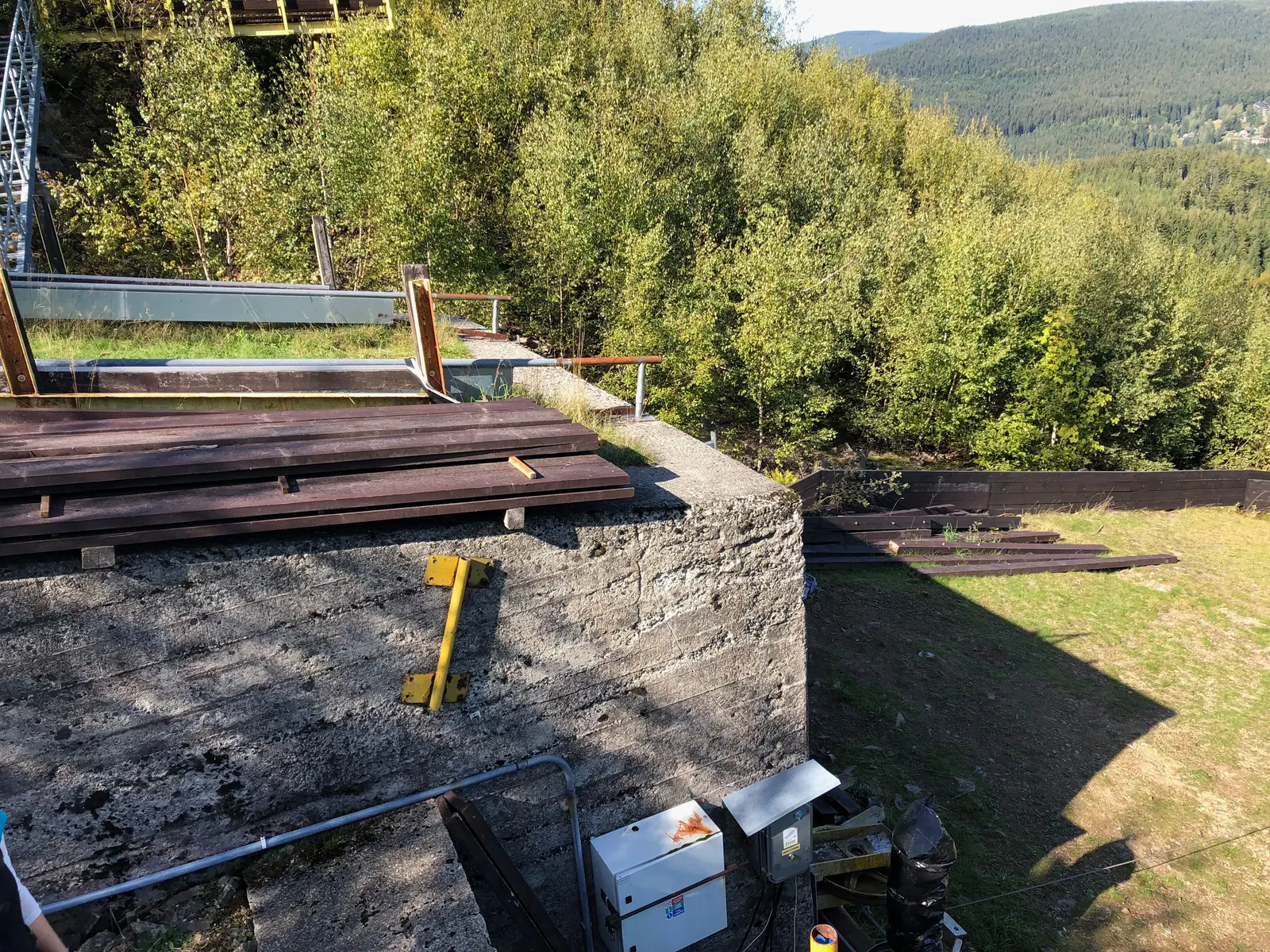 Betonový blok s dřevěnými fošnami, za ním ocelová plošina.
