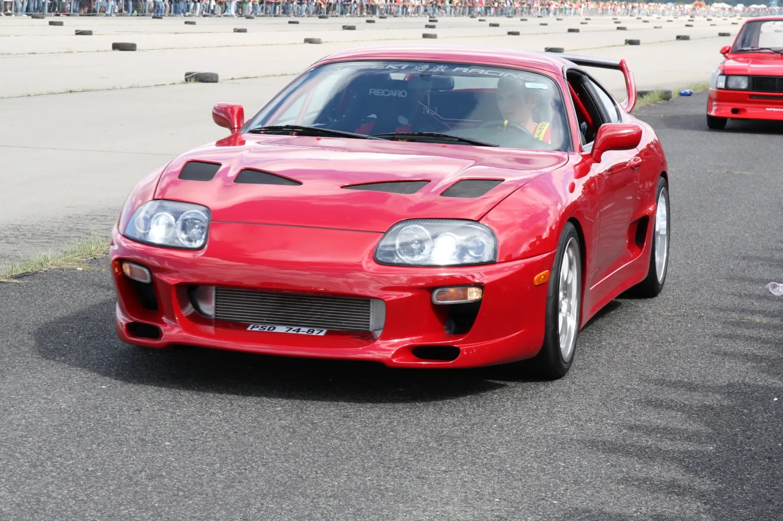 Červená Toyota Supra na sprintové trati před tribunou