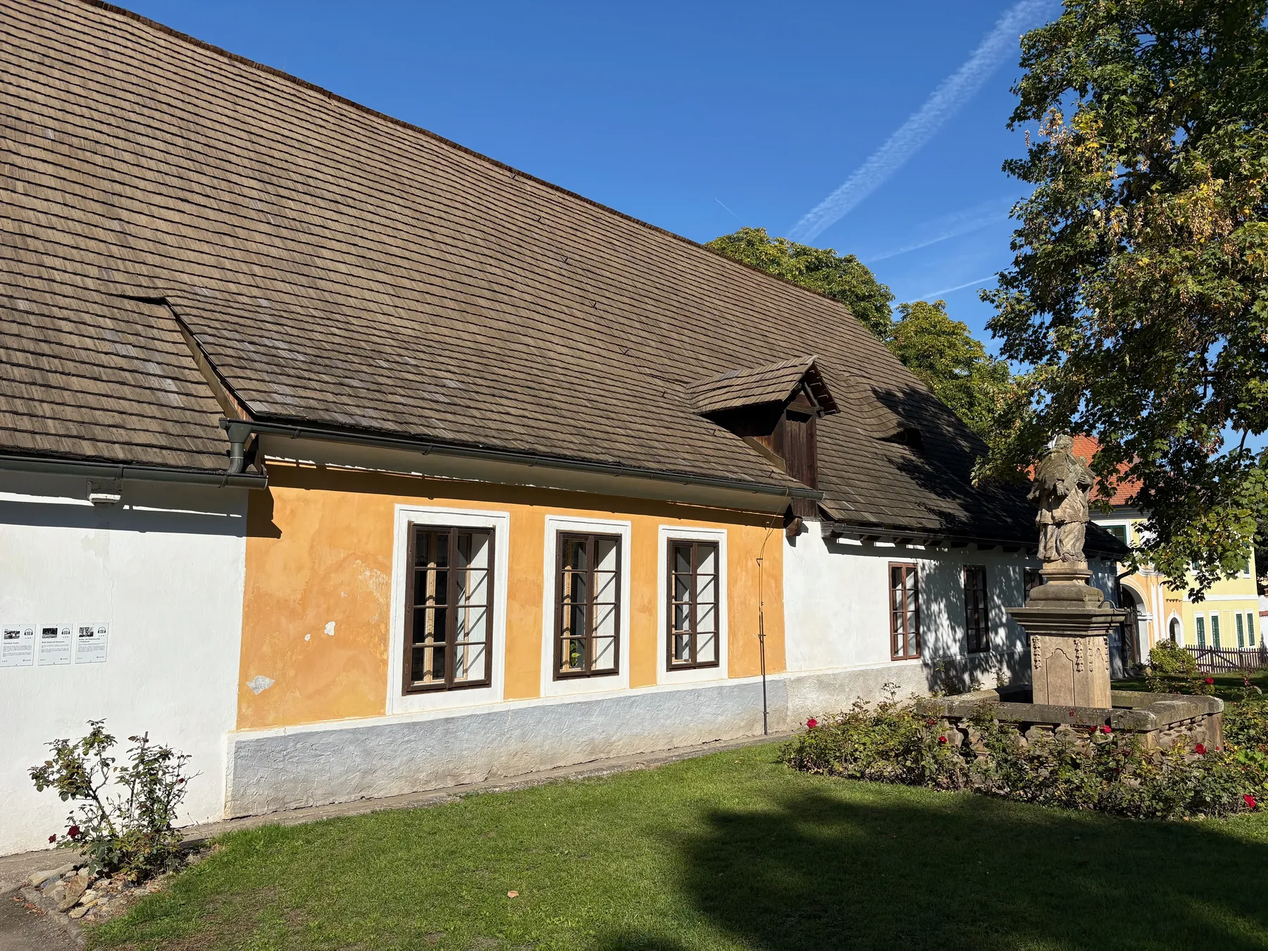 Boční průčelí bednárny s okrovou omítkou, sochou svatého Jana Nepomuckého vpravo, cihlová střecha