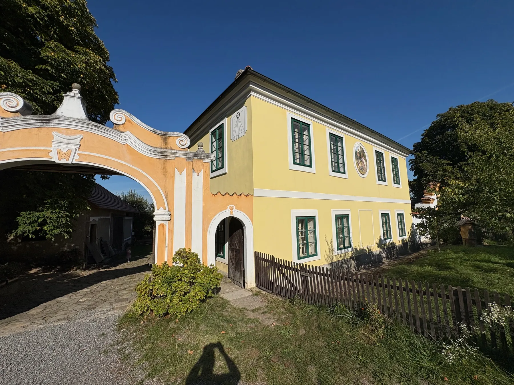 Detail stavby s klasicistní fasádou a barokní branou, zelené okenice