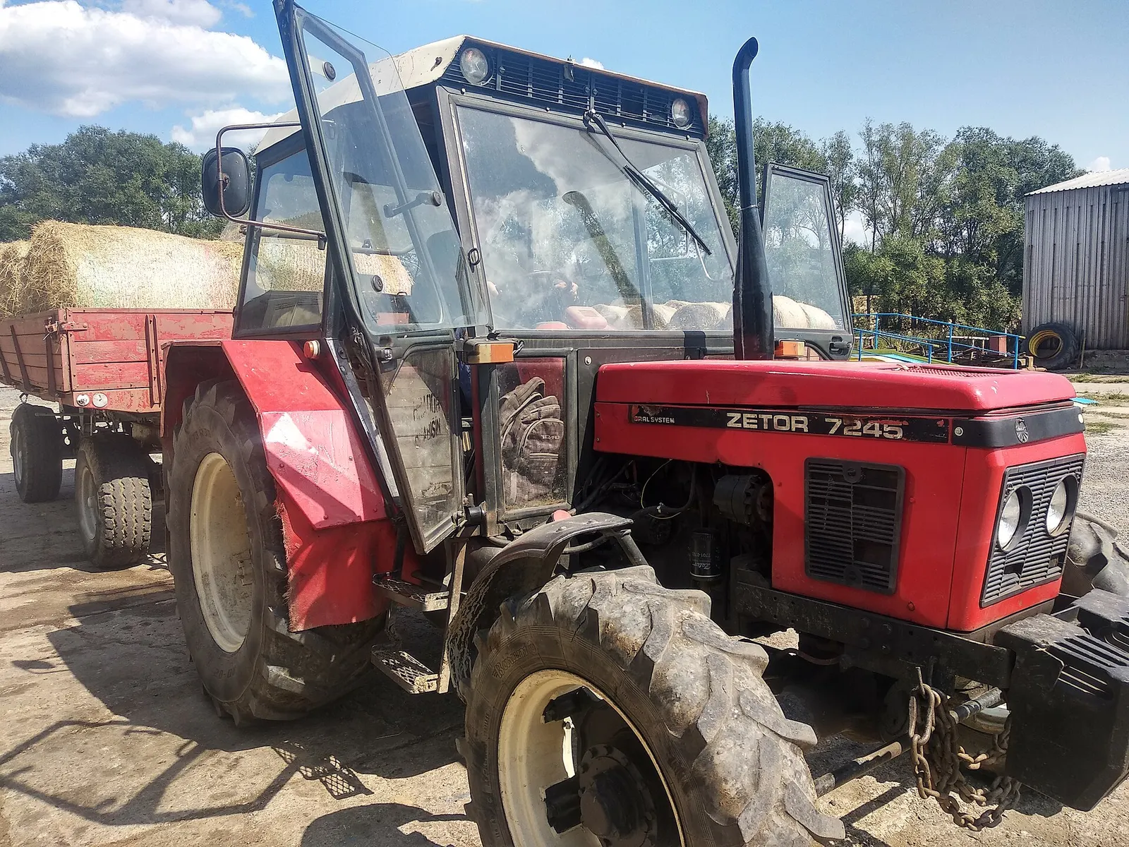 Pracovní Zetor 7245 Horal System s vlekem naloženým balíky sena na dvoře